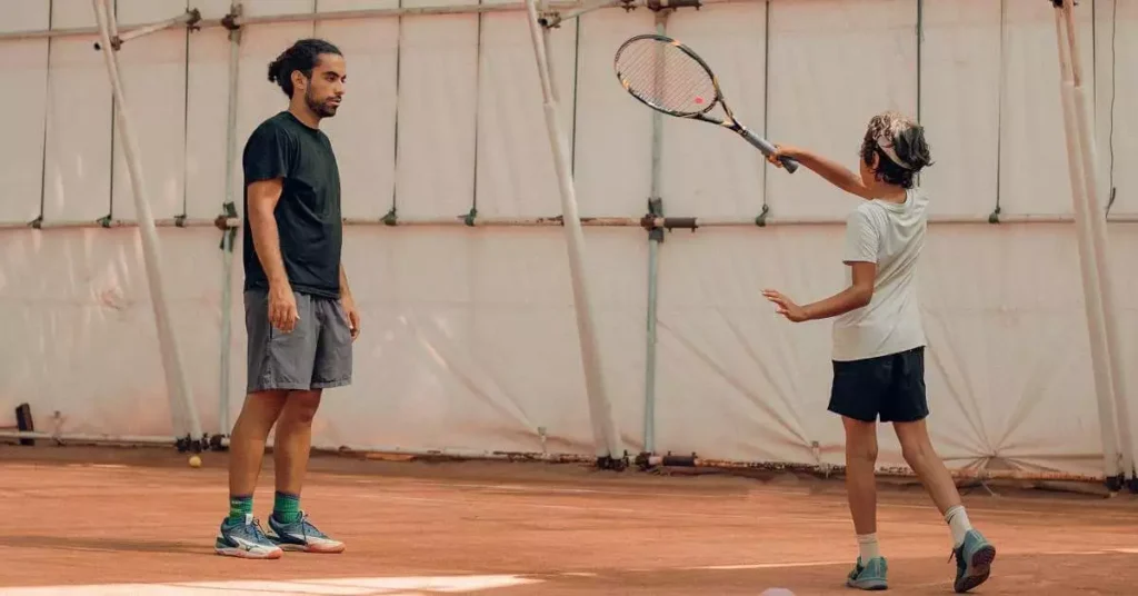 child learning tennis with tennis coach